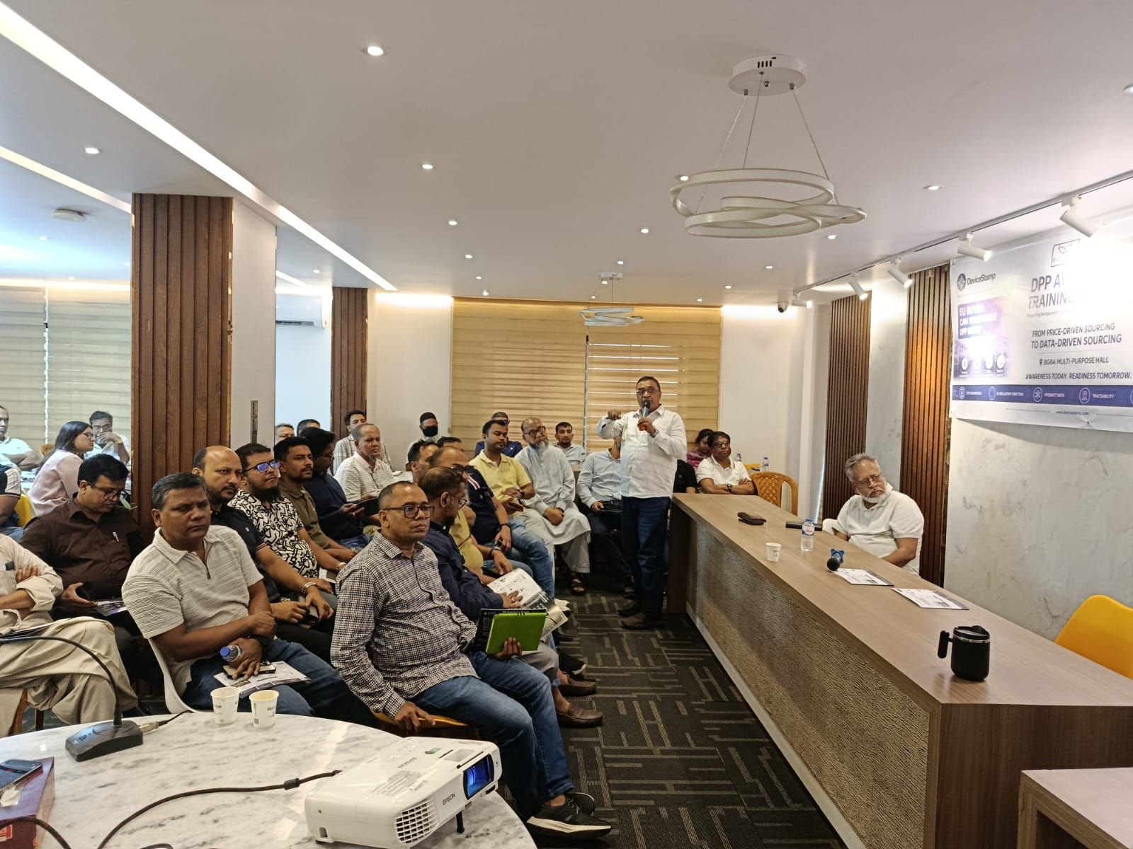 A speaker addresses participants at the BGBA × DeviceStamp DPP Awareness & Training Program 2026 at the BGBA Multipurpose Hall in Uttara, Dhaka
